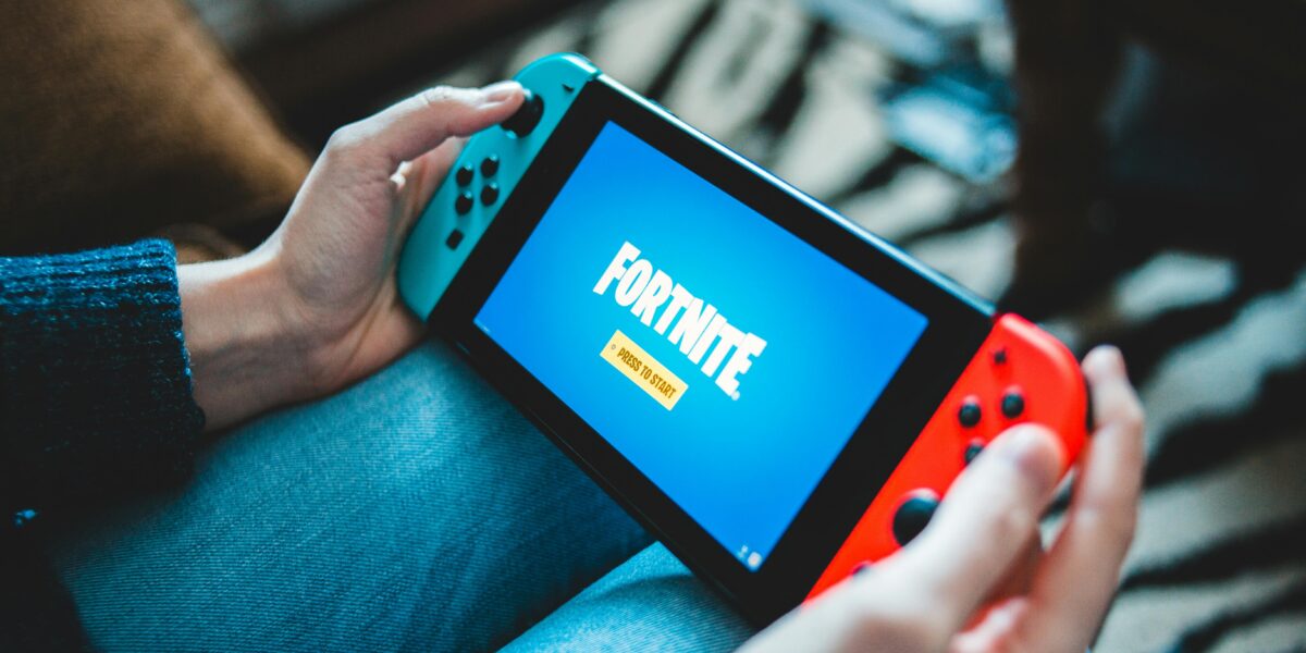 Close-up of hands holding a Nintendo Switch with Fortnite game screen indoors.